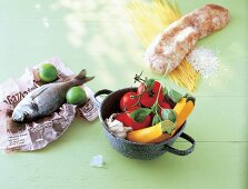 Raw fish and lime on newspaper, vegetables in pot and bread on uncooked spaghetti