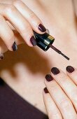 Close-up of woman applying dark violet nail paint on fingernails