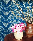 Pussy willow and cyclamen flowers in vase against blue patterned wallpaper