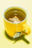 Close-up of yellow cup with teabag on yellow background