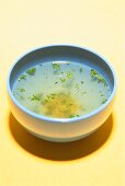 Close-up of broth soup in bowl on yellow background