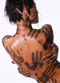Nackter Rücken mit Handabdrücken aus Erde, Frau verteilt Schlamm