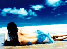 Rear view of woman wearing bikini lying on beach, blurred