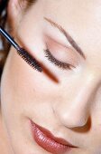 Close-up of woman wearing red lipstick applying mascara on eyelashes, eyes closed