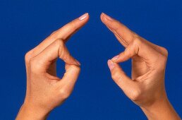 Close- up of woman's hand performing acupressure mudra against blue background