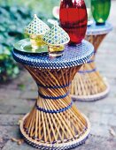 Gläser mit Bambushauben stehen auf einem Hocker aus Bambusgeflecht