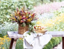 Colourful summer bouquet in wicker basket with napkin and bowl of fruits on side