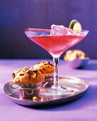 A red cocktail in a glass next to two muffins
