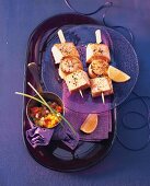 Zwei Fisch-Spieße auf einem Teller mit Zitrone, daneben Paprika-Salsa