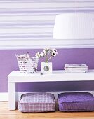 White table with square vase, cushion on wooden surface against striped wall