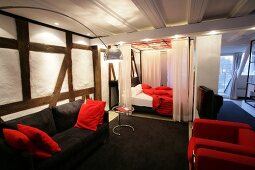 View of room with red sofa and bed, black sofa and white curtains at hotel in Germany