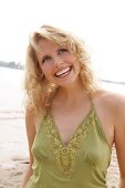 Portrait of beautiful blonde woman wearing green halter top standing on beach, smiling