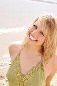 Portrait of beautiful blonde woman wearing green halter top standing on beach, smiling