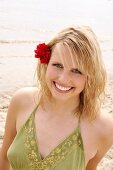 Happy blonde woman with flower in hair wearing green halter top standing on beach, smiling