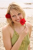 Woman wearing green halterneck dress holding red flower on beach, laughing