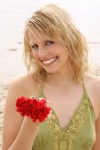 Woman wearing green halterneck dress holding red flower on beach, laughing