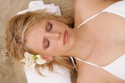 Pretty woman wearing white bikini lying on sand with towel under her head, eyes closed