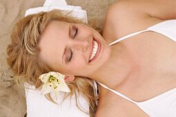 Overhead view of pretty woman in white bikini lying on sand, smiling with eyes closed