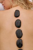 Rear view of blonde woman lying on beach with stones on her back