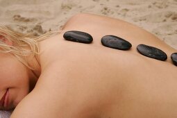 Rear view of blonde woman lying on beach with stones on her back