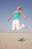 Frau am Strand springt freudig in Luft