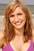 Portrait of beautiful blonde woman wearing pink top standing on beach, smiling