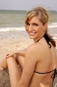 Portrait of beautiful blonde woman sitting on beach, smiling