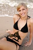 Portrait of pretty woman in black bikini lying on beach with seaweed on her belly, smiling