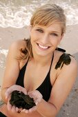 Portrait of attractive woman in black bikini standing on beach with algae in hands