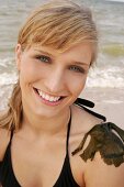Portrait of beautiful woman in black bikini top sitting with seaweed on shoulder, smiling