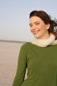 Beautiful woman wearing green sweater, jeans and scarf, standing and smiling