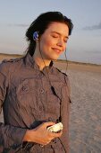 Pretty woman wearing brown shirt and jeans listening music, looking away and smiling