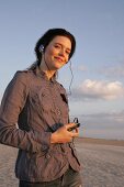 Pretty woman wearing brown shirt and jeans listening music, looking away and smiling