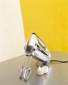 Plastic chromed hand mixer and eggshell on white-yellow background