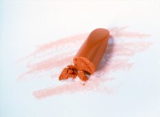 Close-up of orange broken lipstick on white background