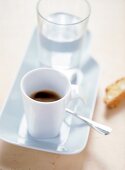 Eine Tasse Kaffe und ein Glas Wasser auf einem schmalen weißen Tablett. x