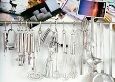 Different kitchen utensils hanging on pole with postcards on wall