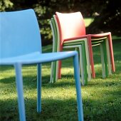 Multi-coloured garden chairs stacked and blue garden chair on lawn