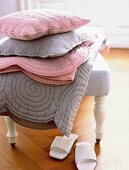Stack of pink and gray quilts and pillows on stool