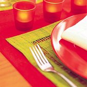 Rote Tischdecke, darauf ein grünes Tischset, Teelichter und eine Gabel
