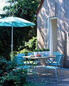 Terrasse vor Holzhaus mit gedecktem Tisch und blauen Stühlen, Schirm