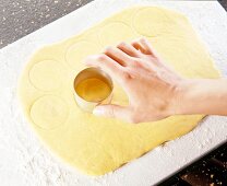 Hand holding round cookie cutter on yellow thick dough