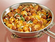 Fried potatoes with onions and bacon in steel pan kept on steel stand