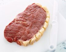 Rohes Steak auf einem Brett, daneben ein Messer.