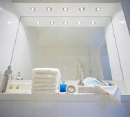 Large mirror over sink with illuminated lights and stacked towel in bathroom