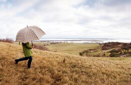 Man holding an umbrella running on meadow in Hiddensee, Germany