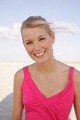 Jennifer Frau mit blonden Haaren trägt pinkes Top u. lacht, am Strand