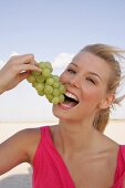Portrait of blonde woman holding bunch of grapes and eating, smiling