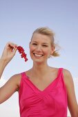 Blonde woman holding a branch of red currants in hand, smiling