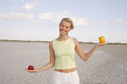 Blonde woman holding an apple in one hand and yellow bell pepper, smiling